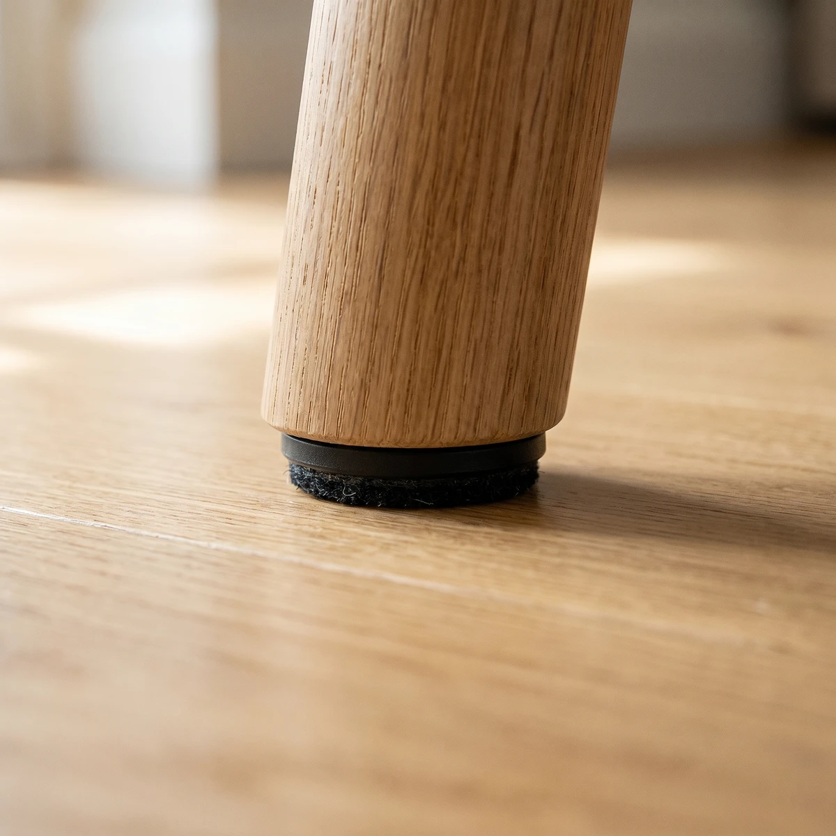 Black furniture glide installed under an oak furniture leg on a hardwood floor
