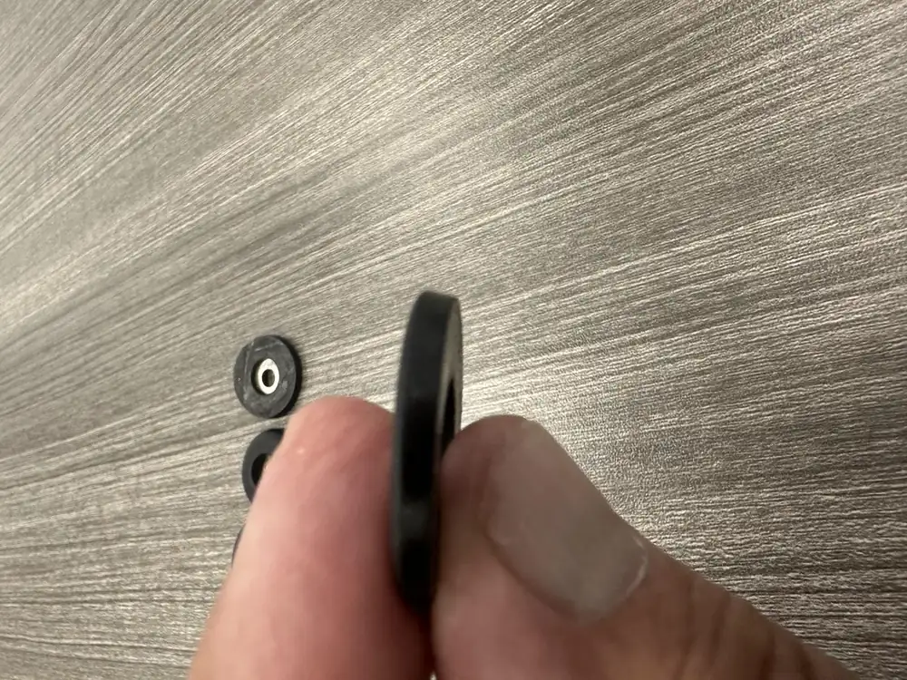 A nail-on furniture glide held in hand beside two worn glides taken off restaurant chairs